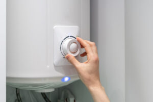 Cropped photo of female adjusting temperature on bathroom electric boiler hanging on wall, using control knob.